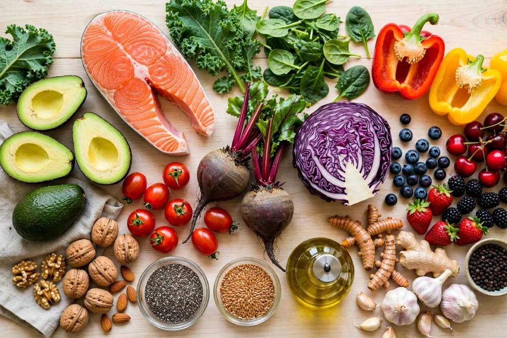 Anti-inflammatory diet foods including salmon, avocado, leafy greens, berries, beets, nuts, turmeric and olive oil on a wooden table